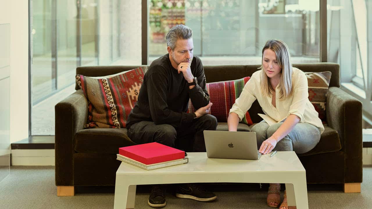 Two work colleagues in a soft area collaborating on something on a laptop